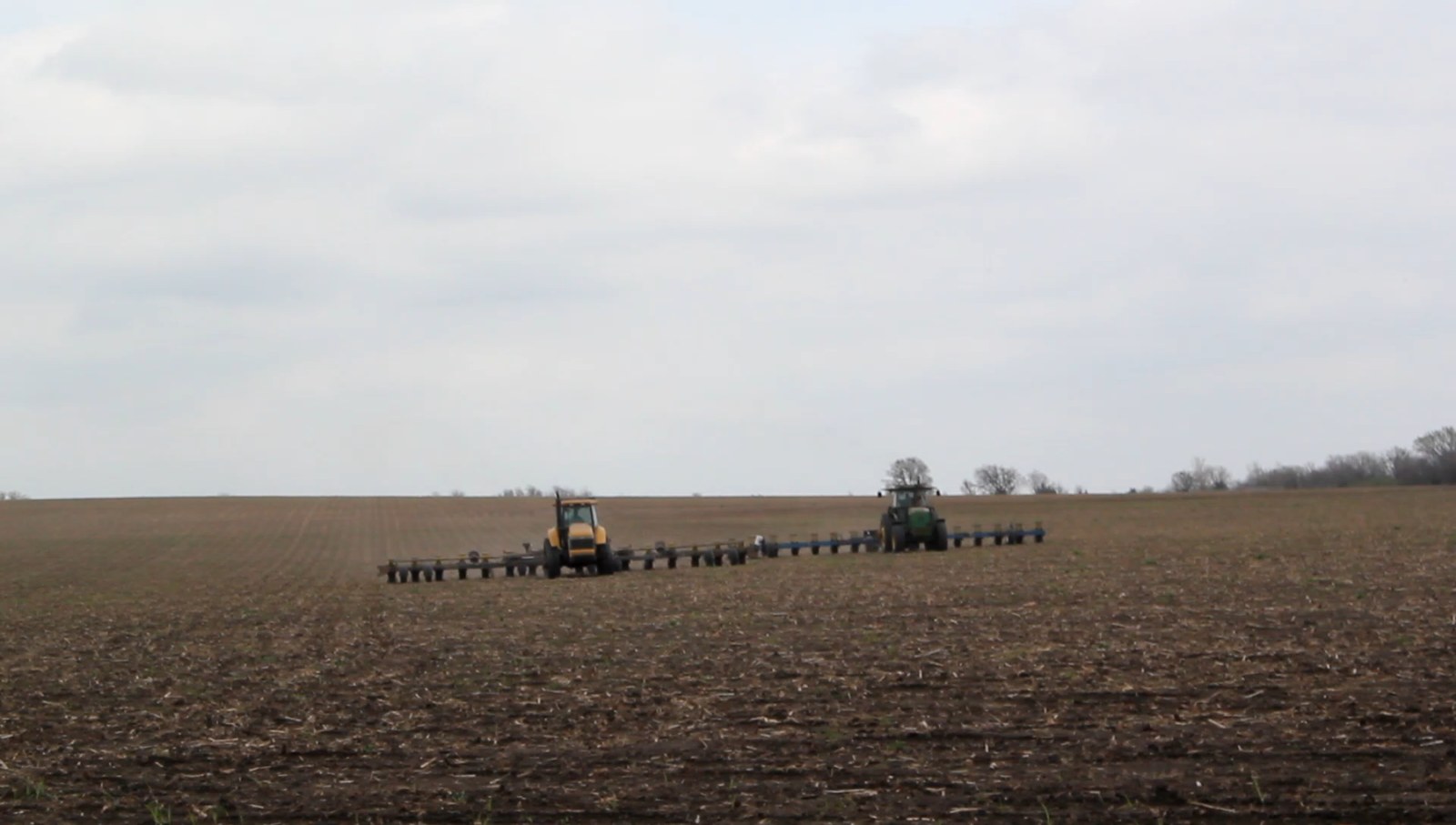 Two tractors running planters side by side across a field, working the ground in line