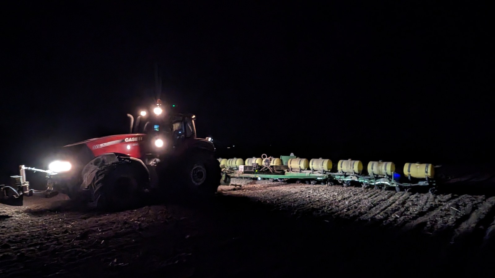 A Case IH tractor pulling a planter across worked ground after dark, its lights on the rows ahead
