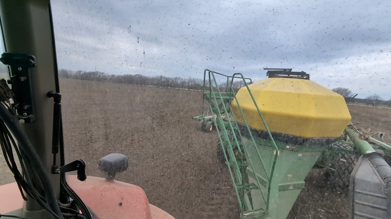 The view back from the cab over the hitch to a green implement with a yellow tank, working through stubble