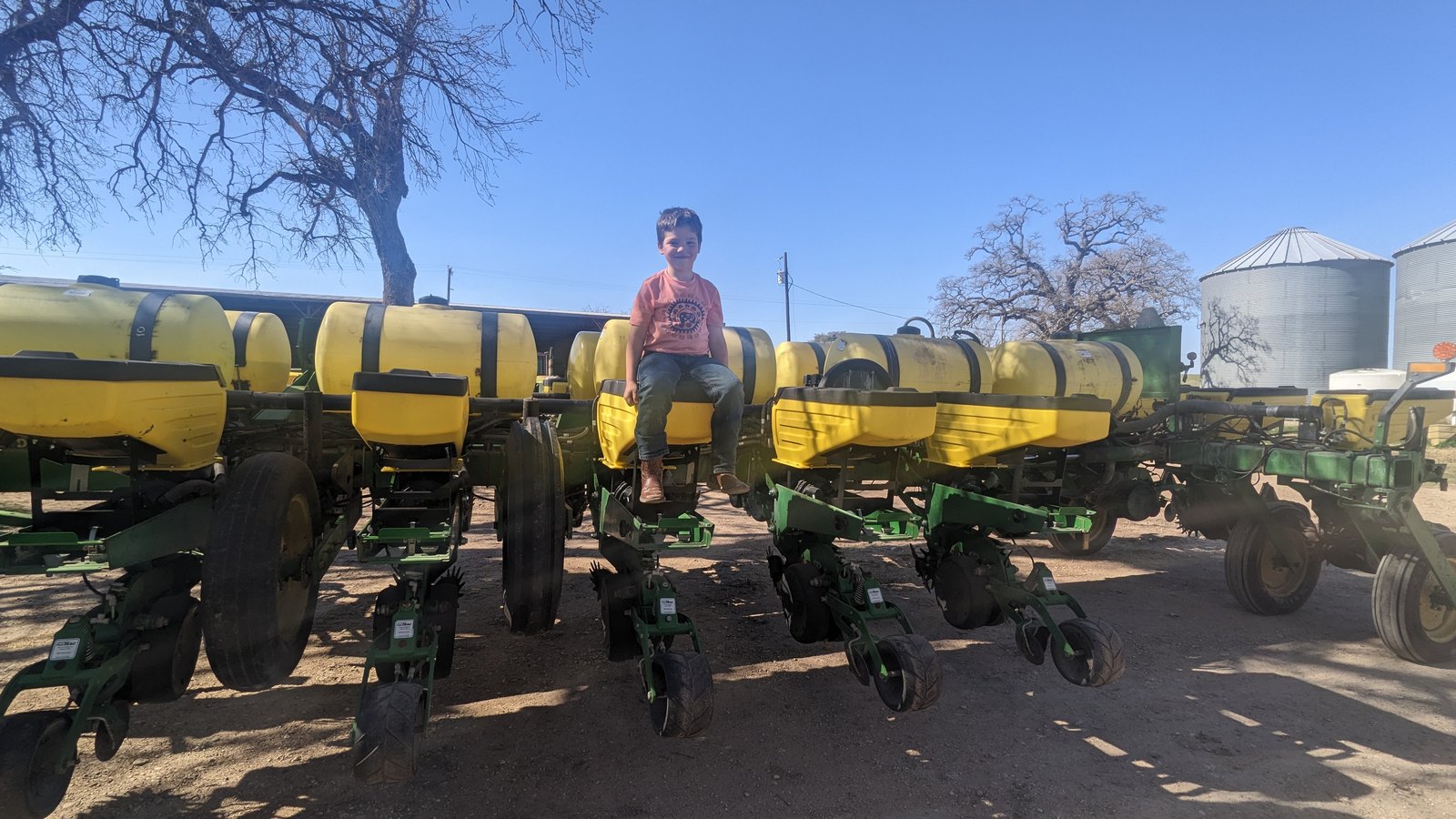 A planter with its seed hoppers in a row, somebody alongside it, grain bins standing behind