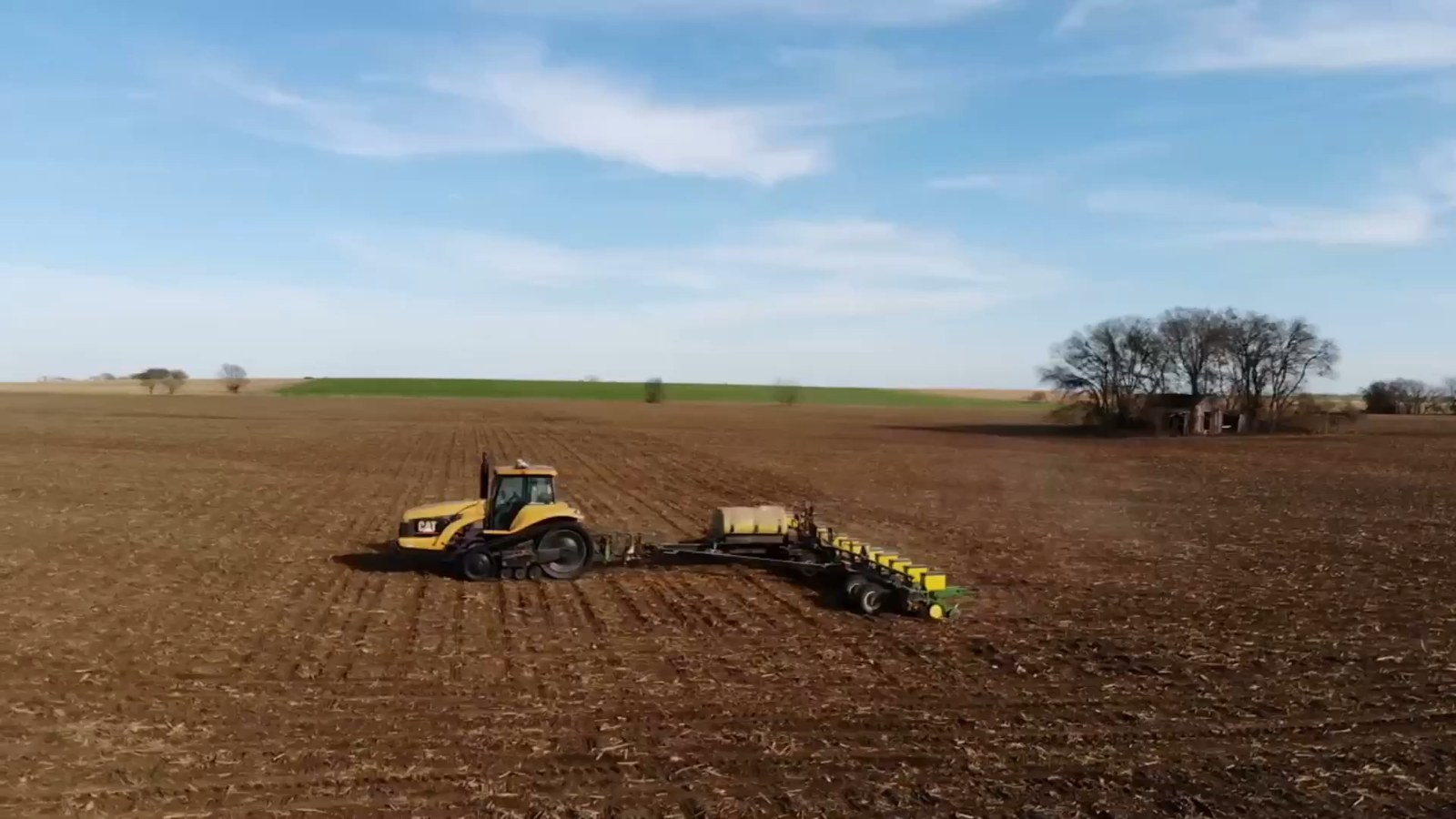 A tracked tractor pulling a planter across a field, the finished rows running out behind it
