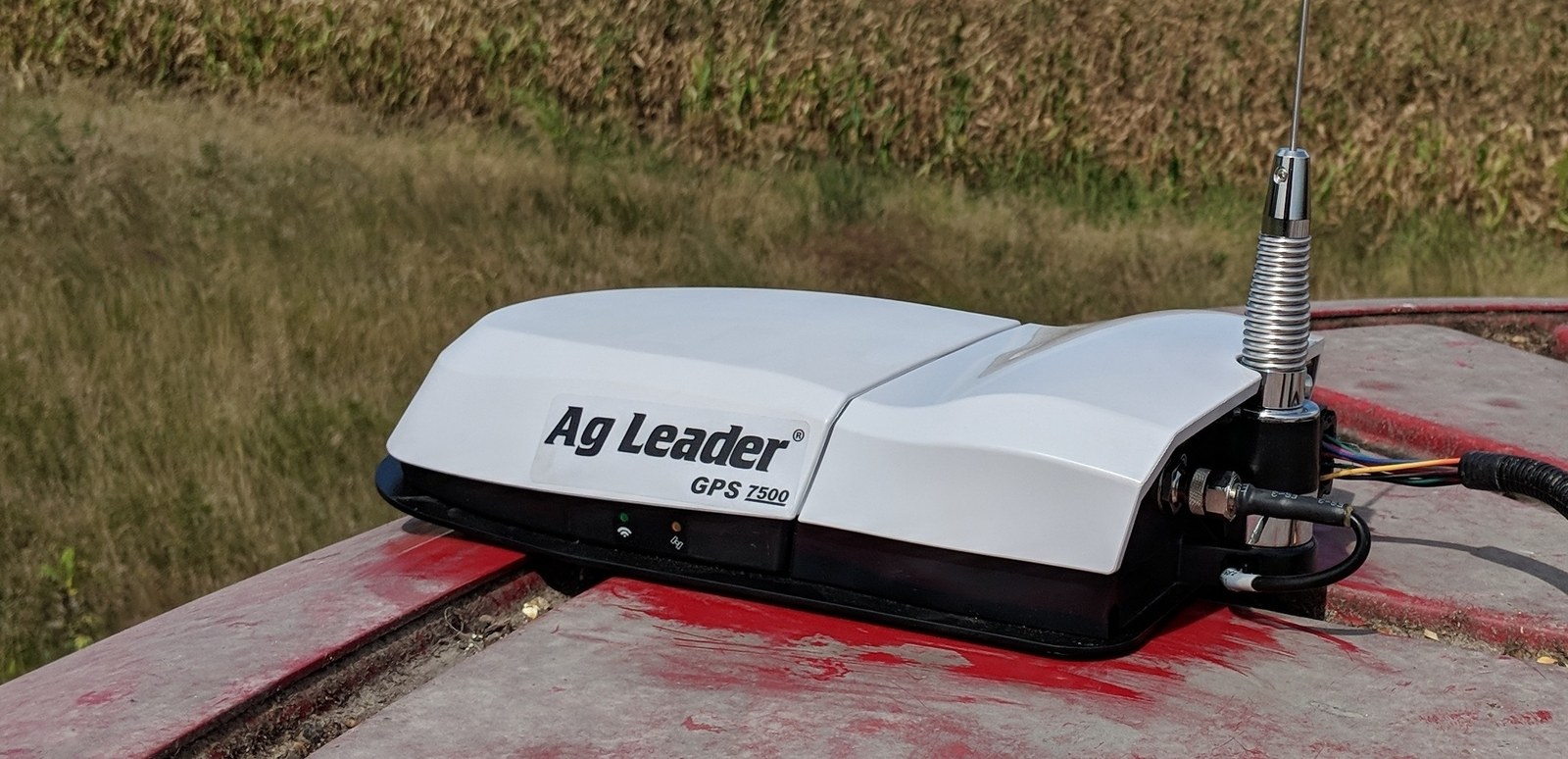 An Ag Leader GPS 7500 receiver mounted on a tractor cab roof, a field of standing corn behind it